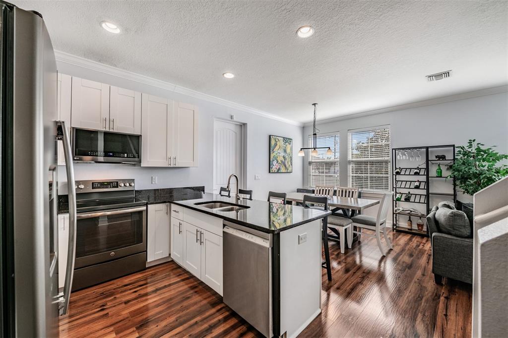 A kitchen with white cabinets, black countertops, stainless steel appliances, and wood-look flooring — 6921 INTERBAY BOULEVARD UNIT 8, TAMPA, FL