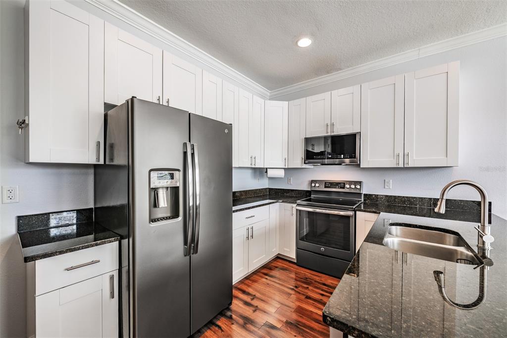 A kitchen features white cabinets, dark granite countertops, stainless steel appliances, and wood flooring — 6921 INTERBAY BOULEVARD UNIT 8, TAMPA, FL