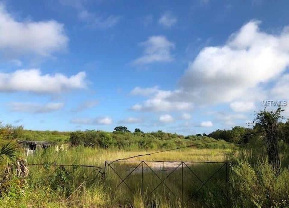 An overgrown, grassy lot features a metal gate and a small, dilapidated structure under a sky — 9221 NEW YORK AVENUE, HUDSON, FL
