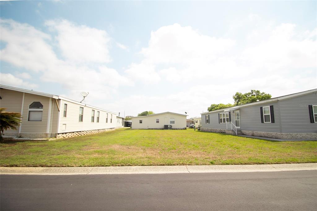 A vacant grassy lot sits between two manufactured homes under a bright, partly cloudy sky — 3024 BRIAR STREET, WESLEY CHAPEL, FL