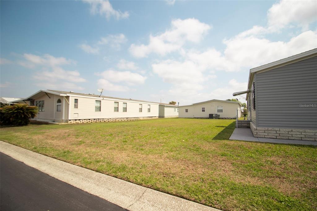 A grassy yard sits between several manufactured homes under a blue sky with clouds — 3024 BRIAR STREET, WESLEY CHAPEL, FL