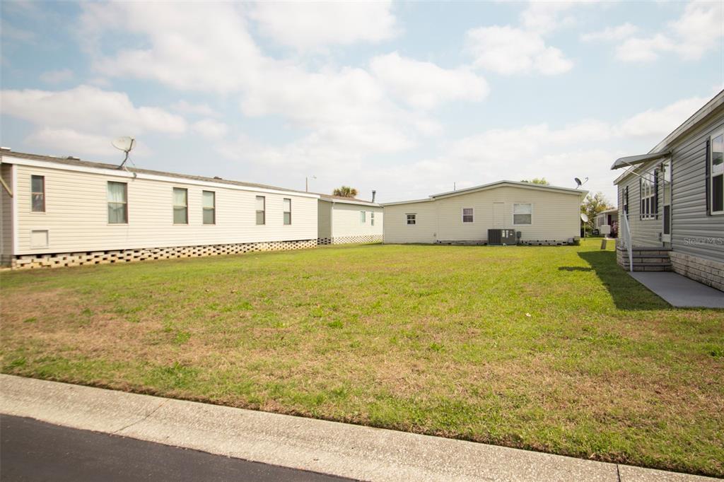 A grassy lot sits between several manufactured homes under a blue sky with clouds — 3024 BRIAR STREET, WESLEY CHAPEL, FL
