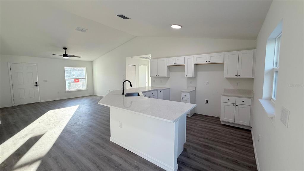 A kitchen with white cabinets, a quartz island, and gray flooring opens to a living area — 2990 TIMBERLAKE, DUNNELLON, FL
