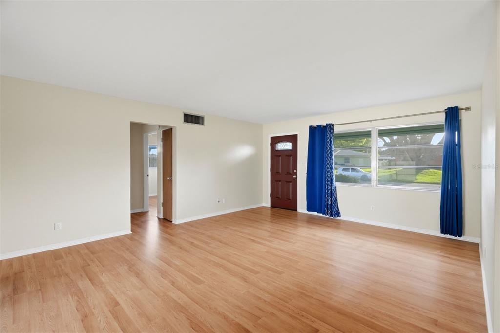 An empty living room features light wood-look flooring, beige walls, a dark door, and windows — 8835 109TH STREET, SEMINOLE, FL
