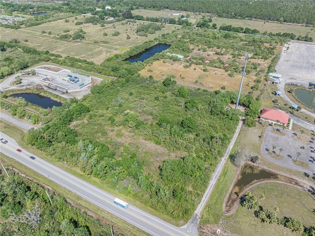 An aerial view shows a vacant, wooded lot situated between a highway and commercial properties — 0 Unassigned, Fellsmere FL 32948, FELLSMERE, FL