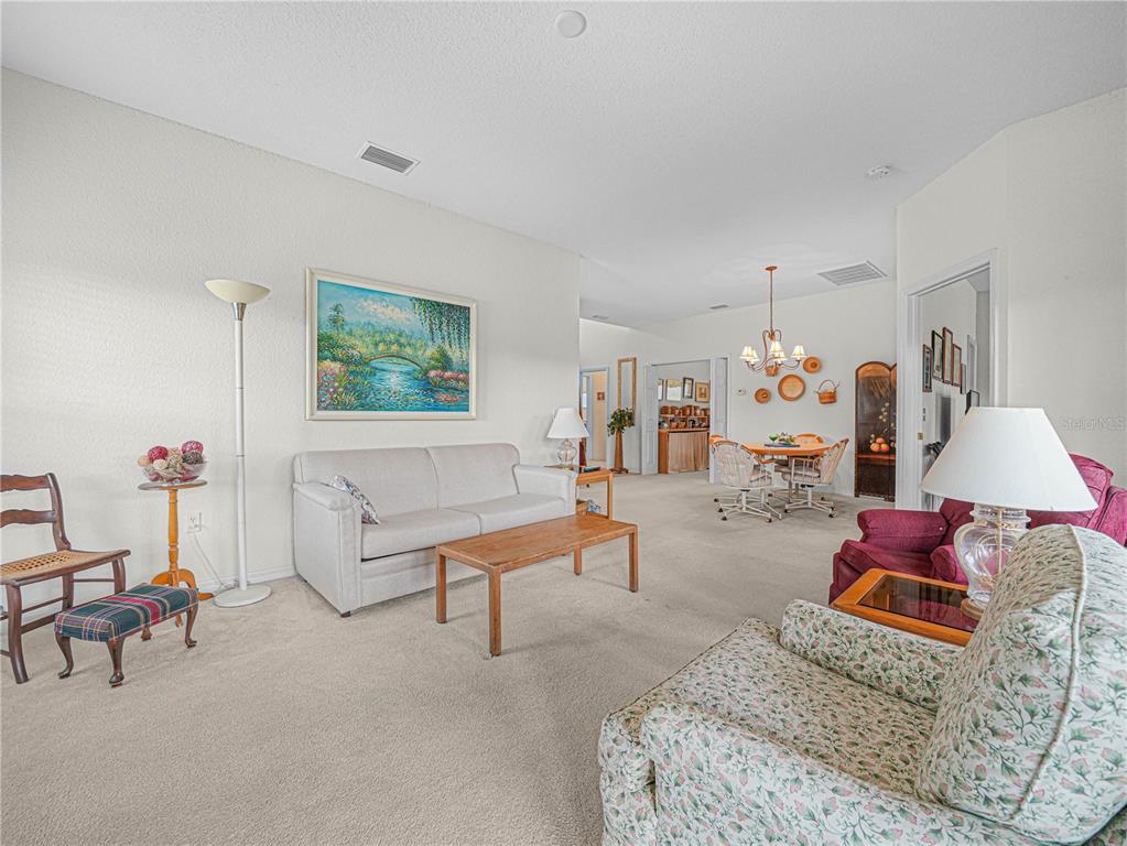 A living room with beige carpet, a light-colored sofa, and a floral armchair — 4251 DORNOCH DRIVE, LAKE WALES, FL