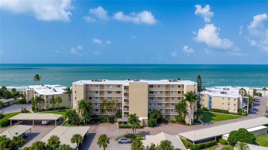 An aerial view shows a multi-story apartment building situated directly along a sandy beach — 4825 GULF OF MEXICO DRIVE UNIT 605, LONGBOAT KEY, FL
