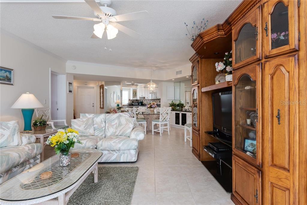 A living room with a large wooden entertainment center, patterned sofa, and an open kitchen — 4825 GULF OF MEXICO DRIVE UNIT 605, LONGBOAT KEY, FL