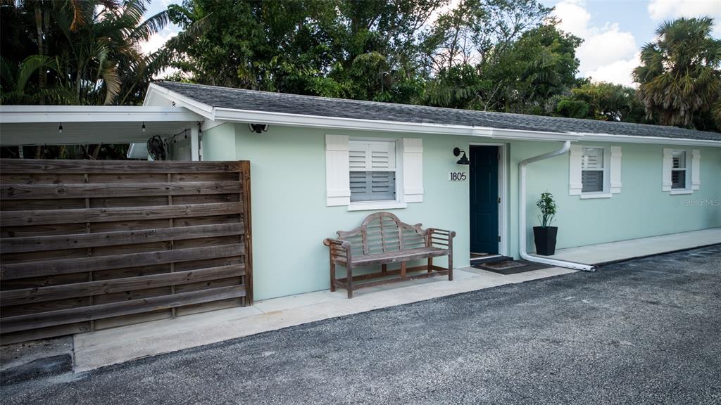 A light green one-story house exterior features a wooden privacy fence, bench, and dark door — 1805 IVANHOE STREET, SARASOTA, FL