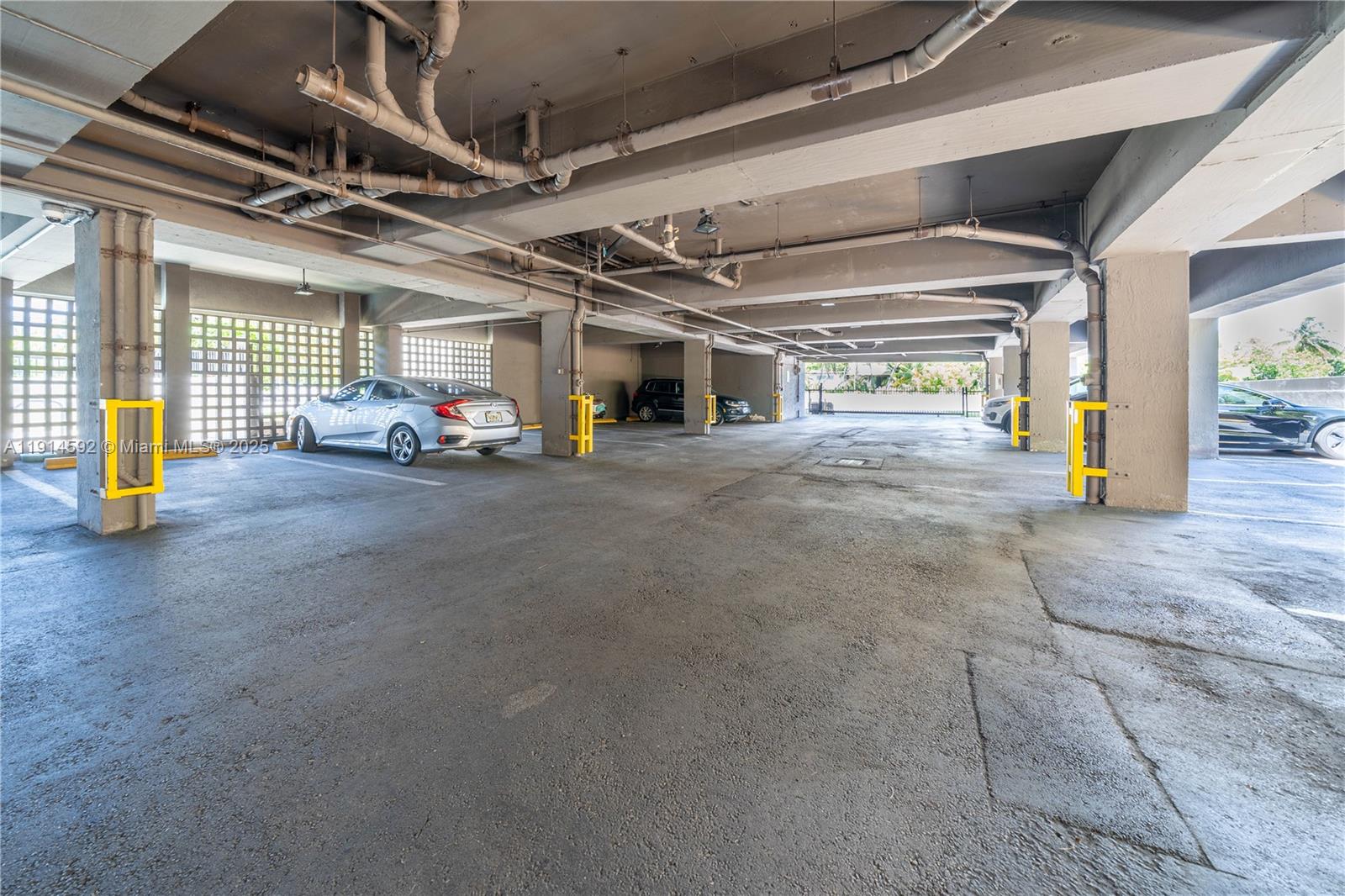 A covered parking garage features concrete pillars, exposed overhead pipes, and several parked cars — 2600 Collins Ave # 308, Miami Beach FL 33140, MIAMI BEACH, FL