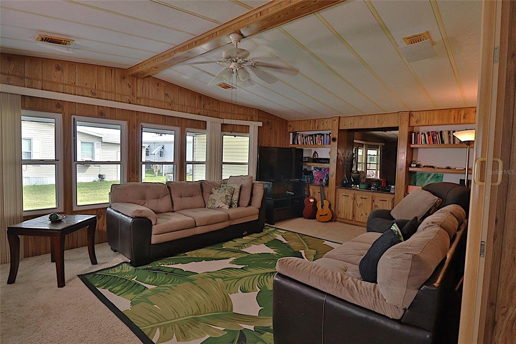 A living room features wood-paneled walls, a ceiling fan, two sofas, and a palm-patterned rug — 3906 CHINABERRY PLACE, COCOA, FL
