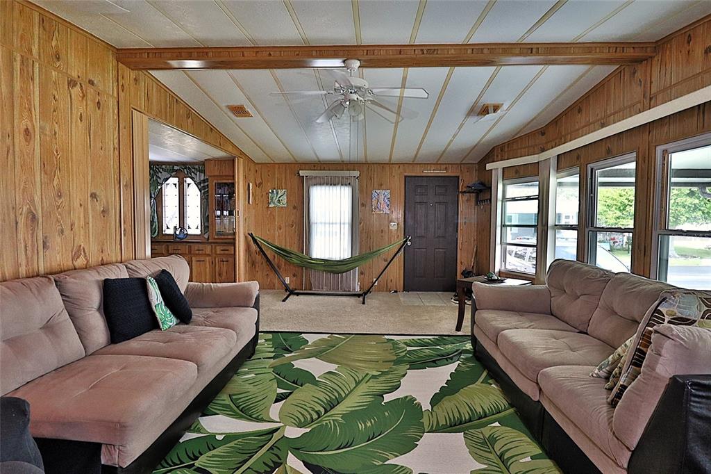 A living room with wood-paneled walls, two sofas, a tropical rug, and an indoor hammock — 3906 CHINABERRY PLACE, COCOA, FL