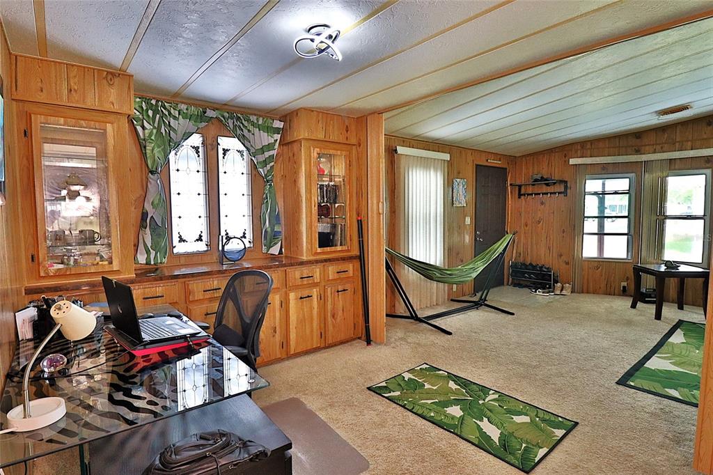 A room with wood-paneled walls, a glass desk, a hammock, and carpeted flooring — 3906 CHINABERRY PLACE, COCOA, FL