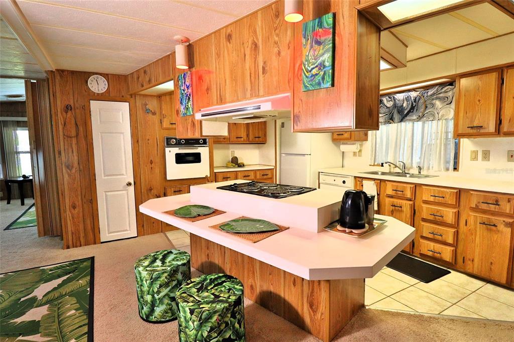 A kitchen with wood paneling, a central island with a cooktop, and light-colored cabinetry — 3906 CHINABERRY PLACE, COCOA, FL