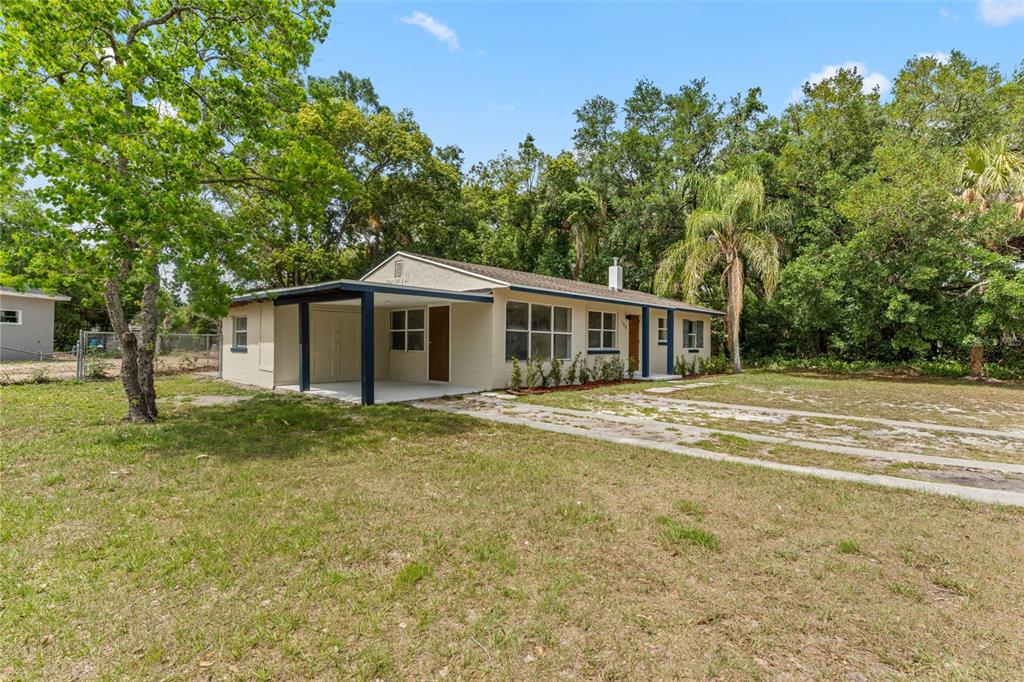 A beige concrete block house features a covered carport with a dark blue support beam — 1218 CRESCENT STREET, SANFORD, FL