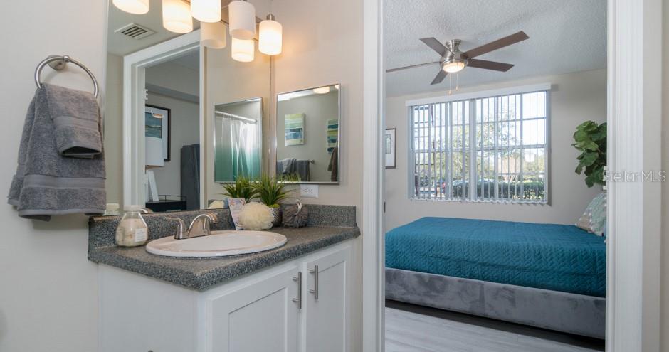 A bathroom vanity with a gray countertop and sink leads into a bedroom with a bed — 1015 OHANA WAY, NORTH PORT, FL