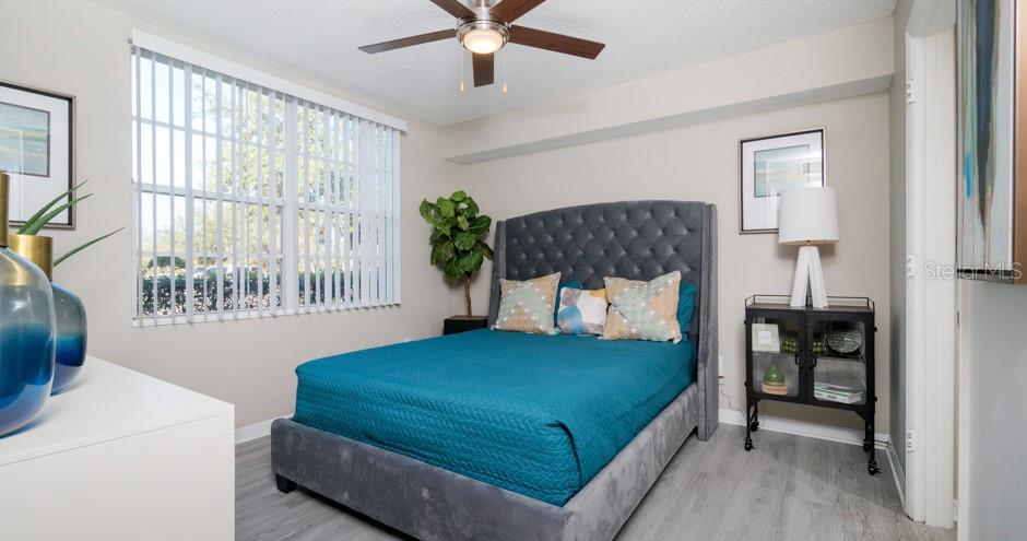 A bedroom features a tufted gray headboard, a teal bedspread, and a ceiling fan — 1015 OHANA WAY, NORTH PORT, FL