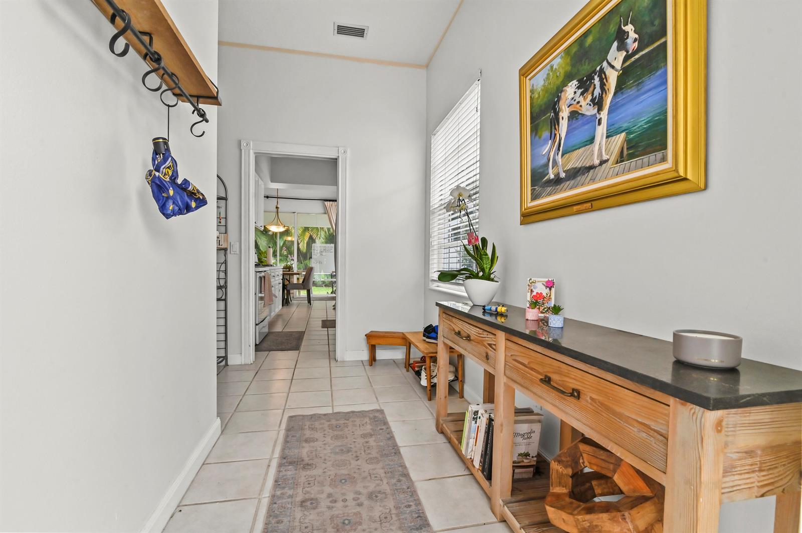 A hallway features a wooden console table, a dog painting, and a doorway to a kitchen — 4766 Valencia Drive, Delray Beach FL 33445, DELRAY BEACH, FL