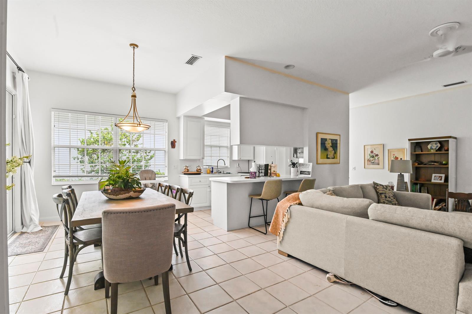 An open-concept living and dining area features tile flooring, a kitchen island, and white cabinetry — 4766 Valencia Drive, Delray Beach FL 33445, DELRAY BEACH, FL