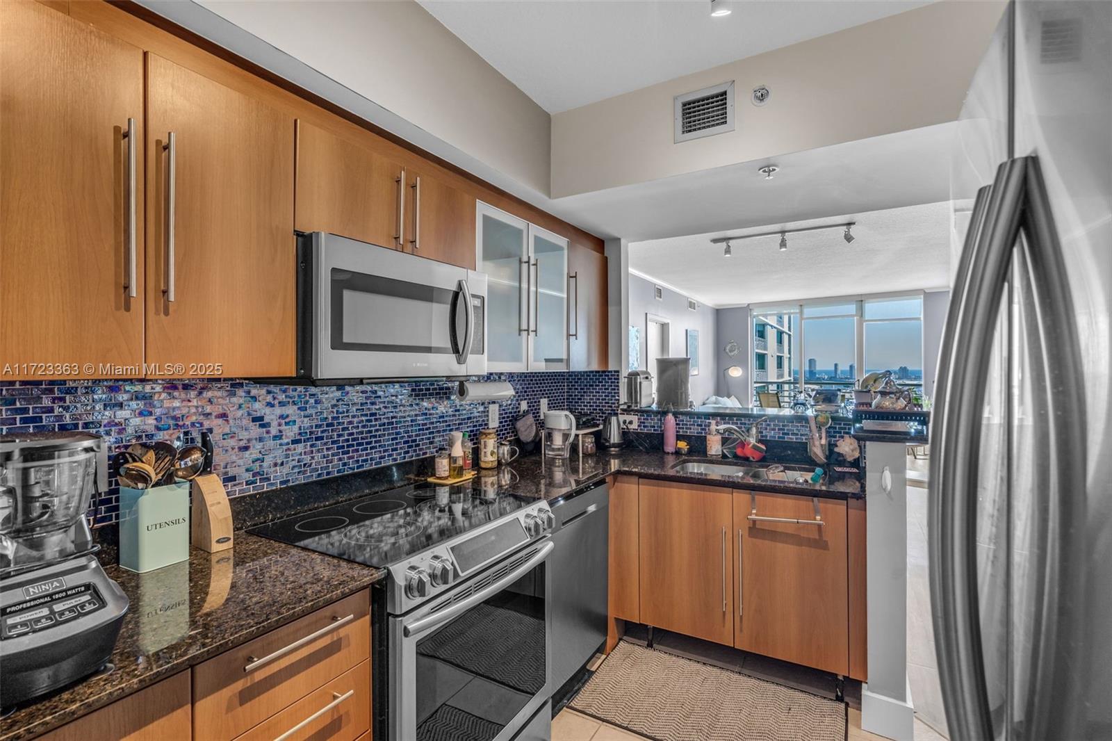 A kitchen features wood cabinets, granite countertops, a blue mosaic backsplash, and stainless steel appliances — 325 S Biscayne Blvd # 3726, Miami FL 33131, MIAMI, FL