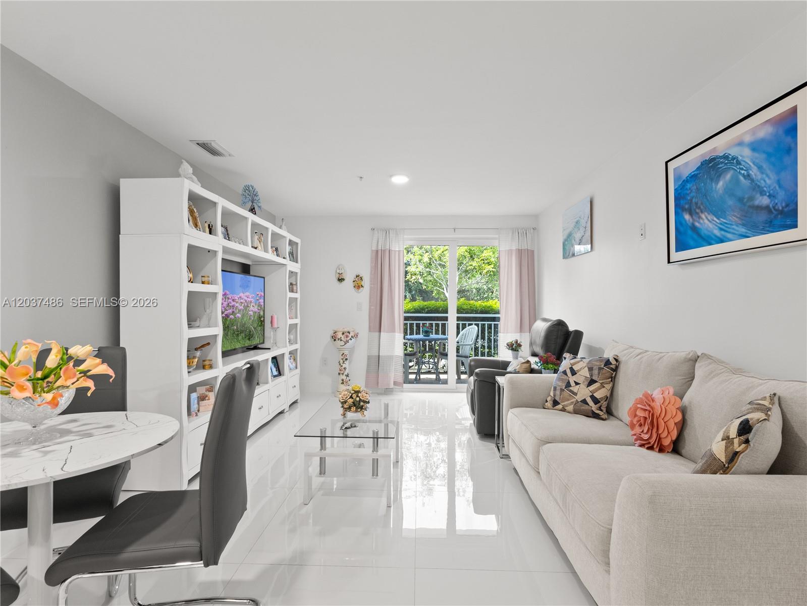 A bright living room features white tile floors, a large entertainment unit, and a balcony view — 10950 NW 82nd St # 115, Doral FL 33178, DORAL, FL