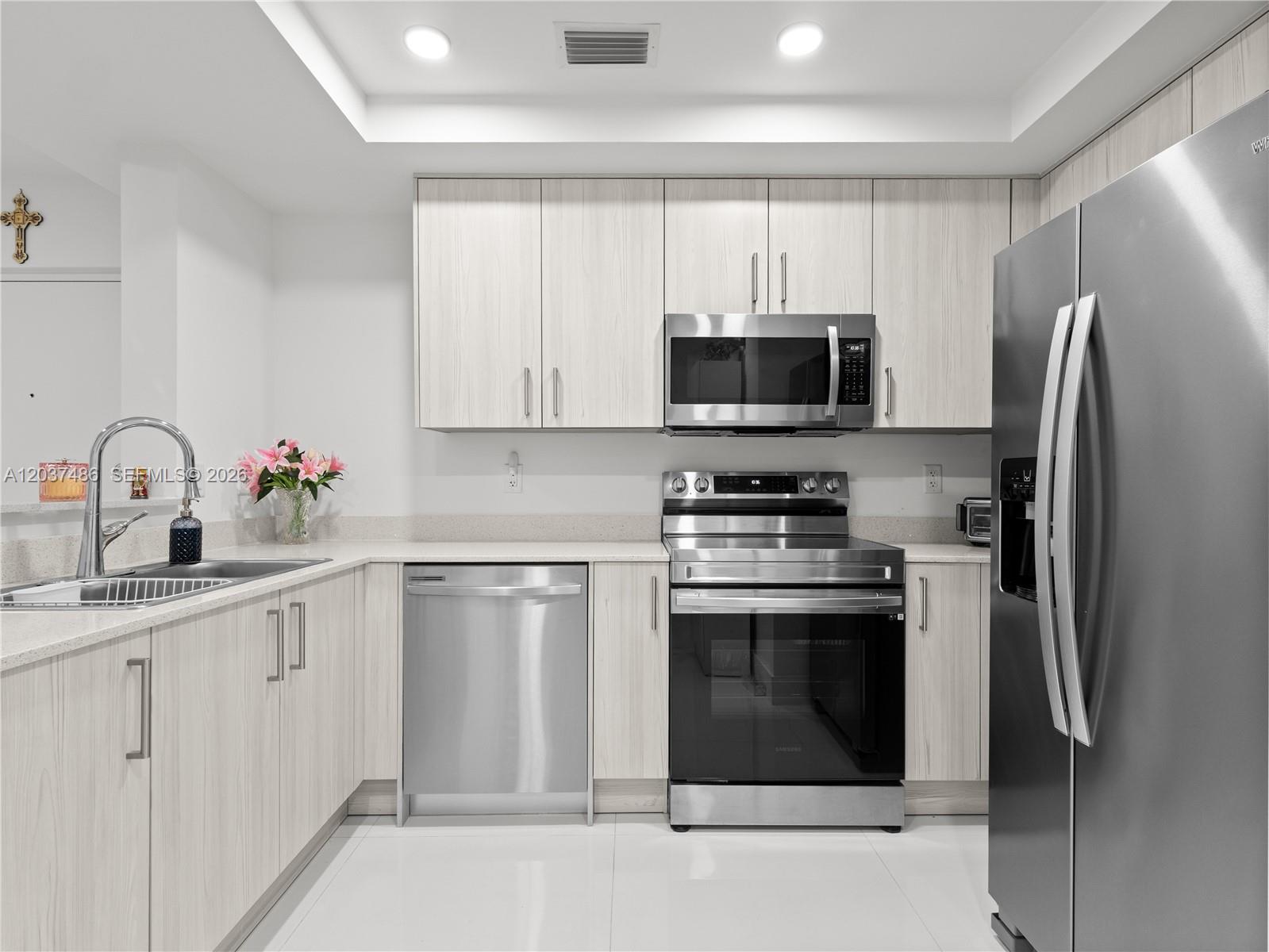 A modern kitchen features light wood cabinets, stainless steel appliances, and white countertops — 10950 NW 82nd St # 115, Doral FL 33178, DORAL, FL