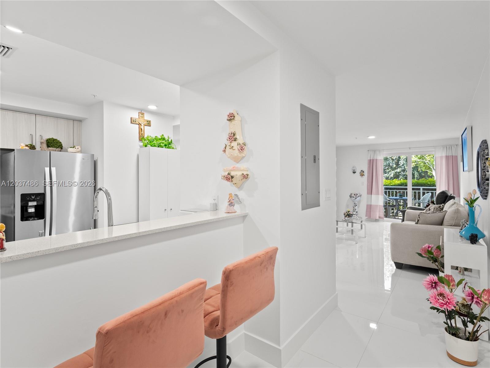 A kitchen with a breakfast bar and stools opens into a bright, white-tiled living area — 10950 NW 82nd St # 115, Doral FL 33178, DORAL, FL