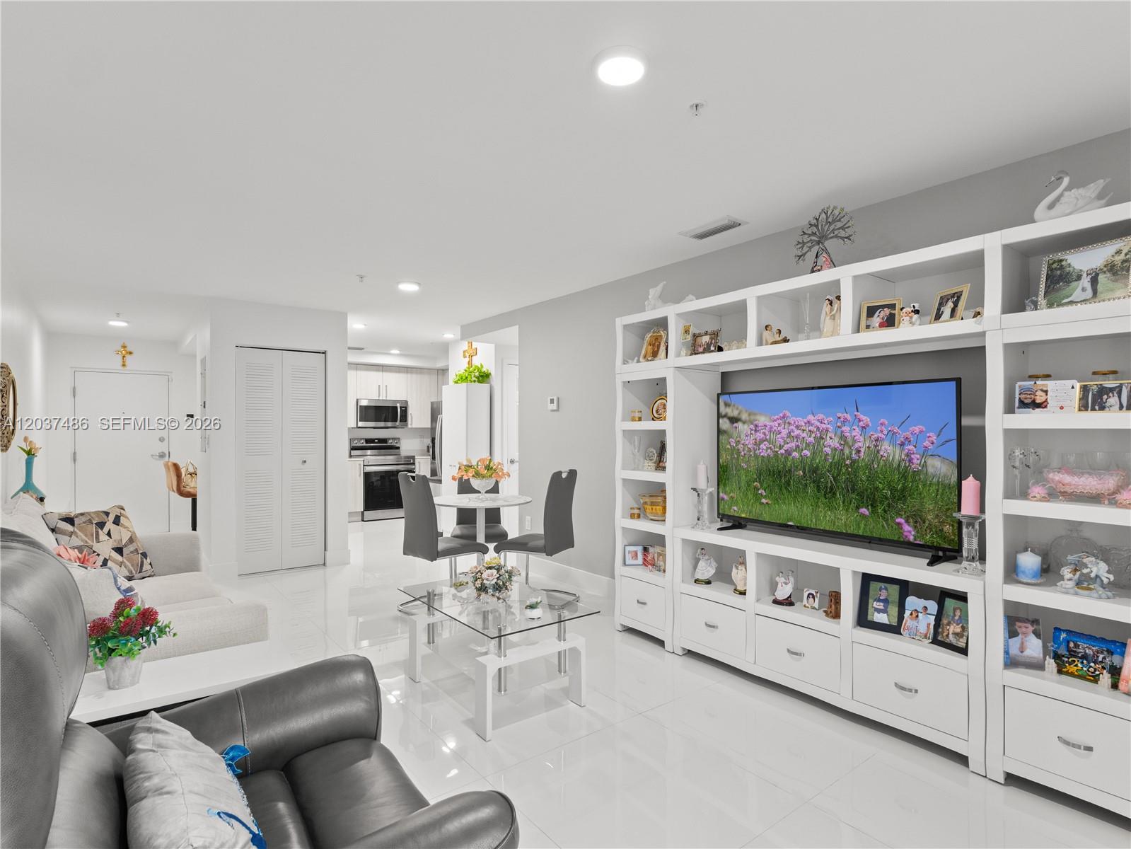 A living room features white tile floors, a large entertainment center, and an open kitchen — 10950 NW 82nd St # 115, Doral FL 33178, DORAL, FL