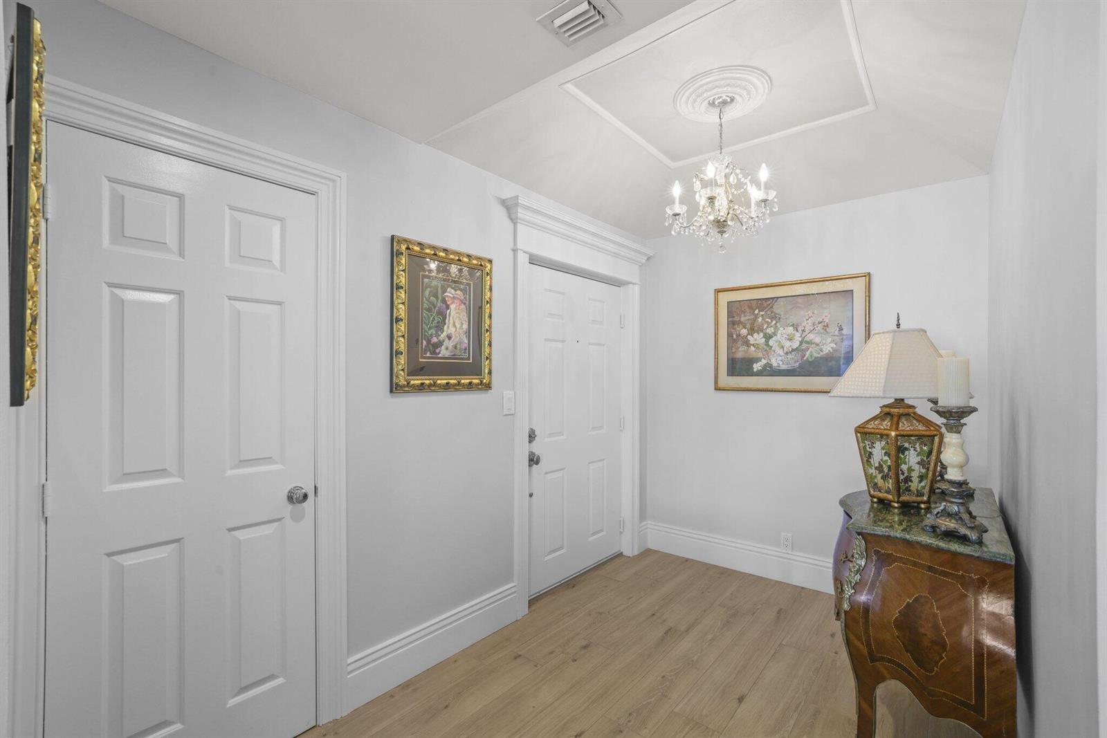 An entryway features light wood flooring, a crystal chandelier, and a decorative wooden chest — 2150 S Ocean Boulevard # 3c, Delray Beach FL 33483, DELRAY BEACH, FL
