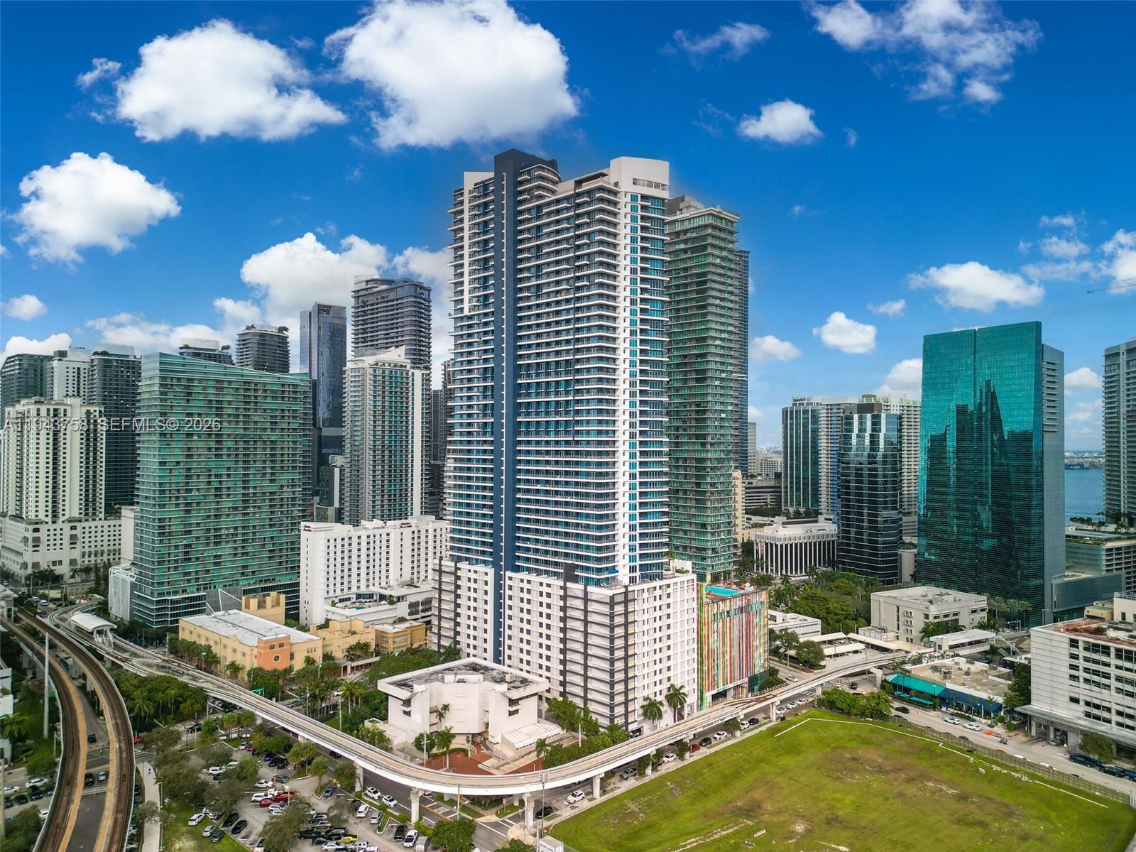 An aerial view shows a tall residential skyscraper surrounded by other high-rise buildings and transit tracks — 60 SW 13th St # 2812, Miami FL 33130, MIAMI, FL