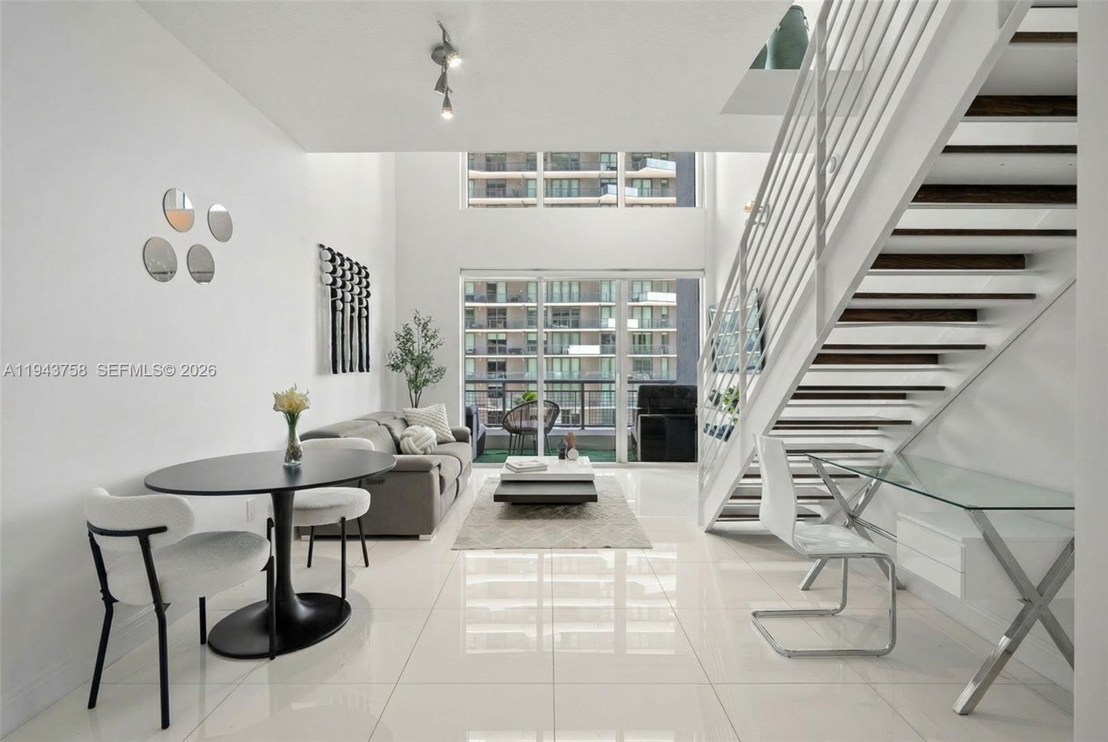 A modern living room features white tile floors, a staircase, and floor-to-ceiling windows — 60 SW 13th St # 2812, Miami FL 33130, MIAMI, FL