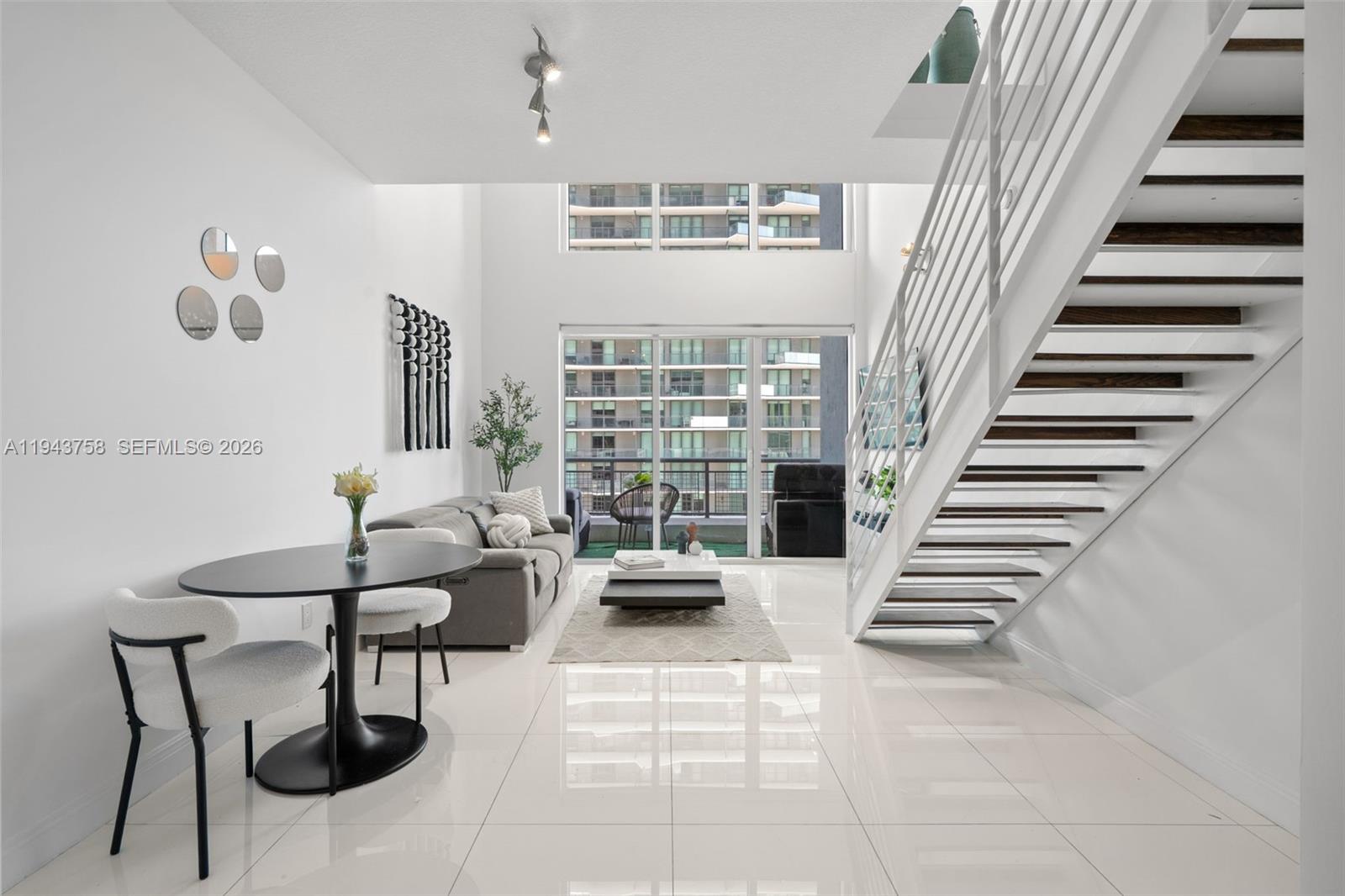 A modern living room features a floating staircase, floor-to-ceiling windows, and white tile flooring — 60 SW 13th St # 2812, Miami FL 33130, MIAMI, FL