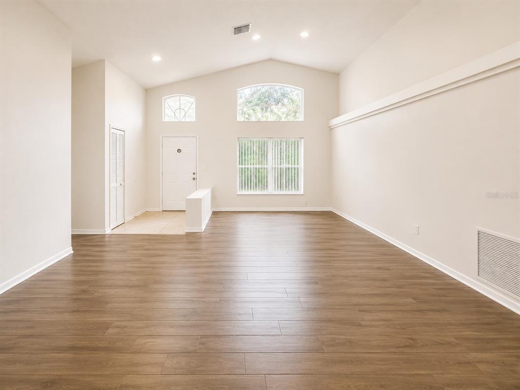 A spacious living room features vaulted ceilings, wood-look flooring, and large windows — 1004 BECKSTROM DRIVE, OVIEDO, FL