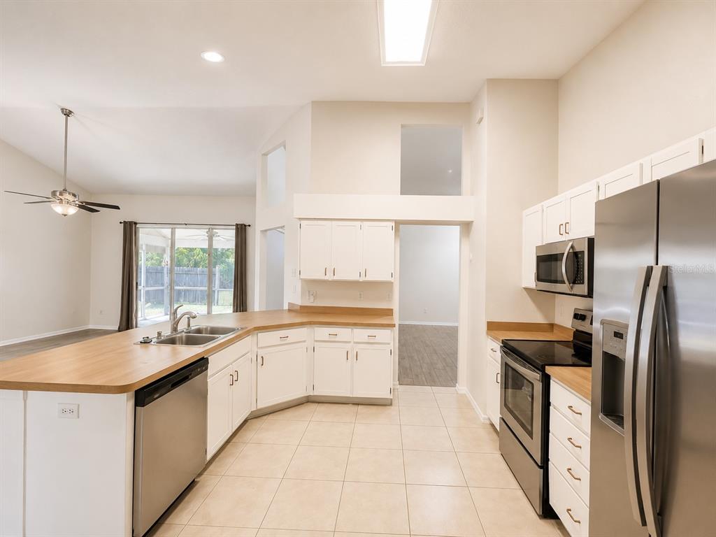 A kitchen with white cabinets, wood-look countertops, stainless steel appliances, and tile flooring — 1004 BECKSTROM DRIVE, OVIEDO, FL