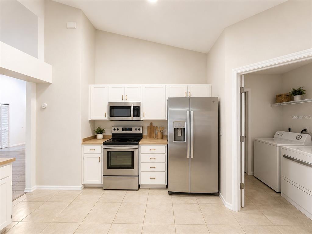 A kitchen with white cabinets, stainless steel appliances, and tile flooring, adjacent to a laundry room — 1004 BECKSTROM DRIVE, OVIEDO, FL