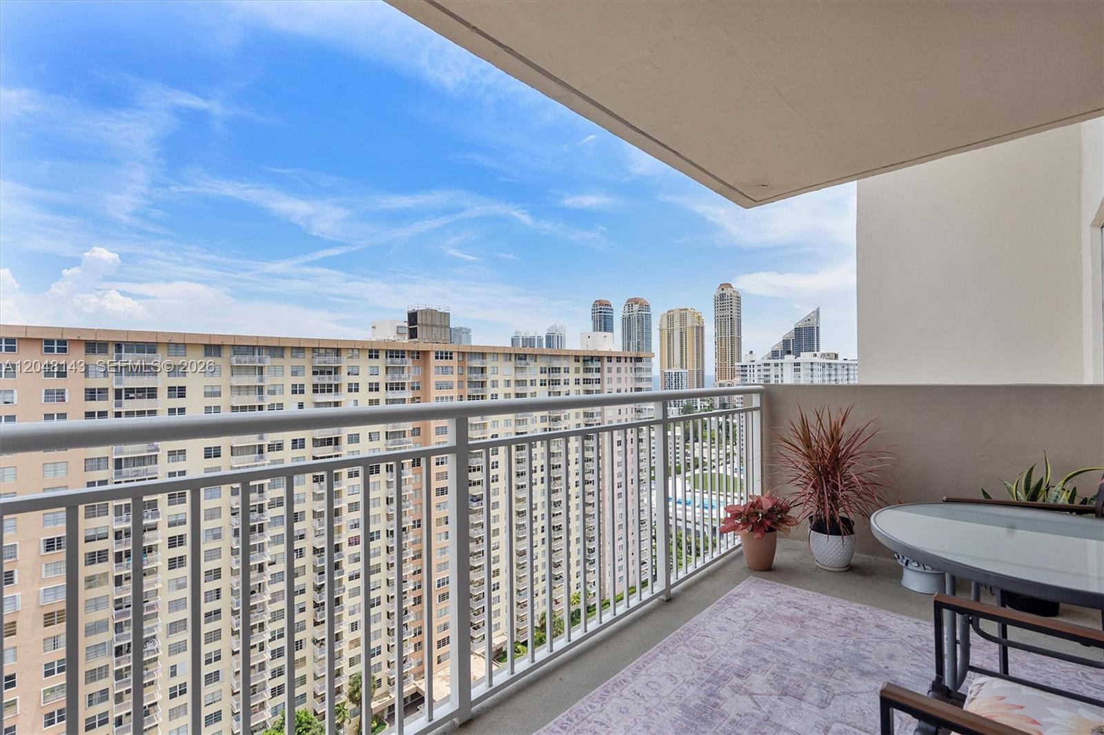 A balcony with a white railing overlooks a dense urban skyline under a blue sky — SUNNY ISLES BEACH, FL