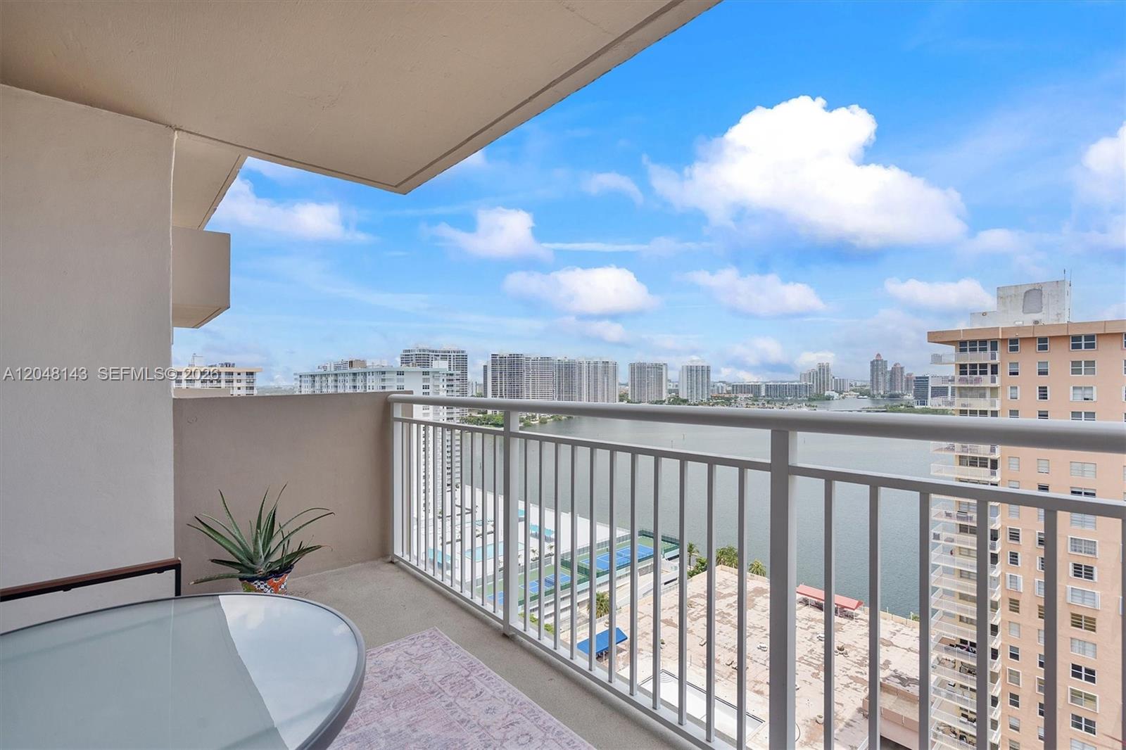 A balcony with a glass table, a potted plant, and a view of the water — SUNNY ISLES BEACH, FL