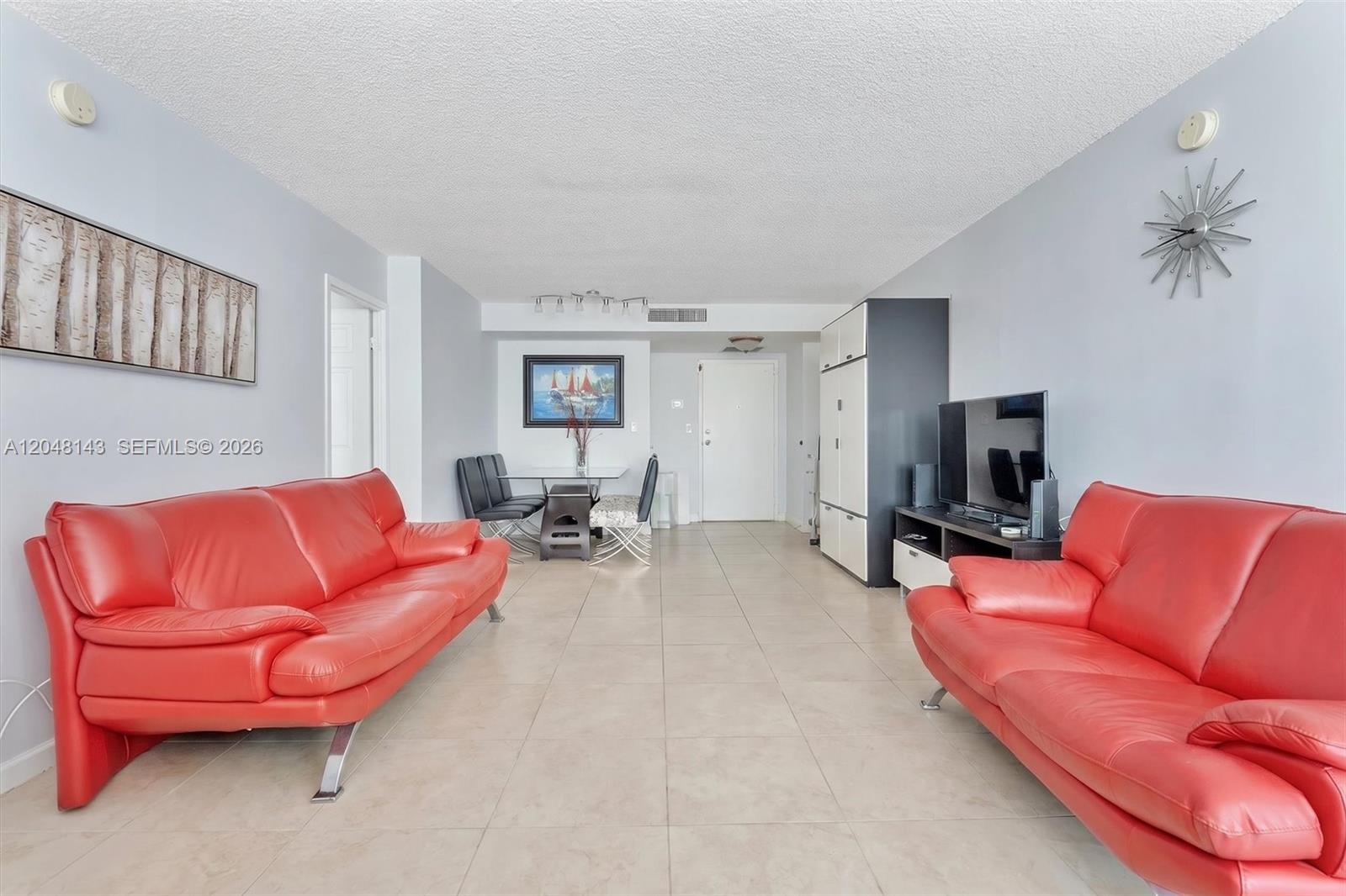 A living room features two red leather sofas, tile flooring, and a dining area — SUNNY ISLES BEACH, FL