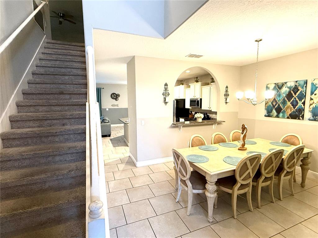 A dining area with a table and chairs sits beside a staircase and kitchen pass-through — 5294 WILDWOOD WAY, DAVENPORT, FL