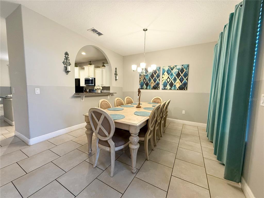 A dining room features a wooden table with six chairs, a chandelier, and teal curtains — 5294 WILDWOOD WAY, DAVENPORT, FL