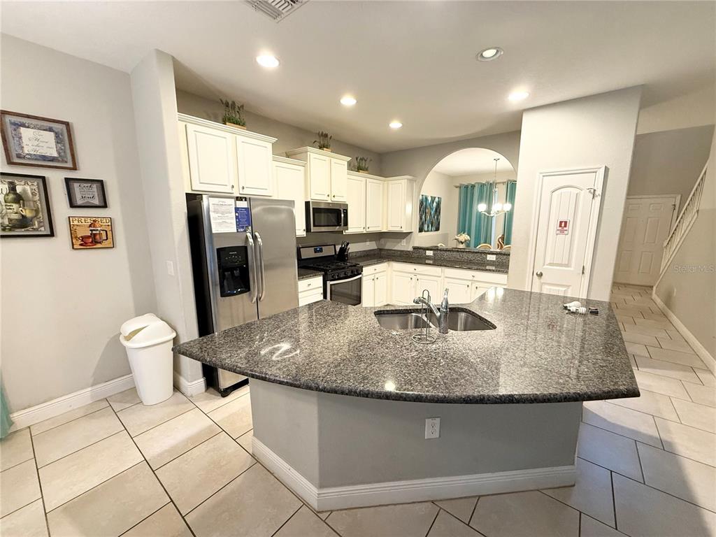 A kitchen features white cabinets, granite countertops, a stainless steel refrigerator, and tile flooring — 5294 WILDWOOD WAY, DAVENPORT, FL