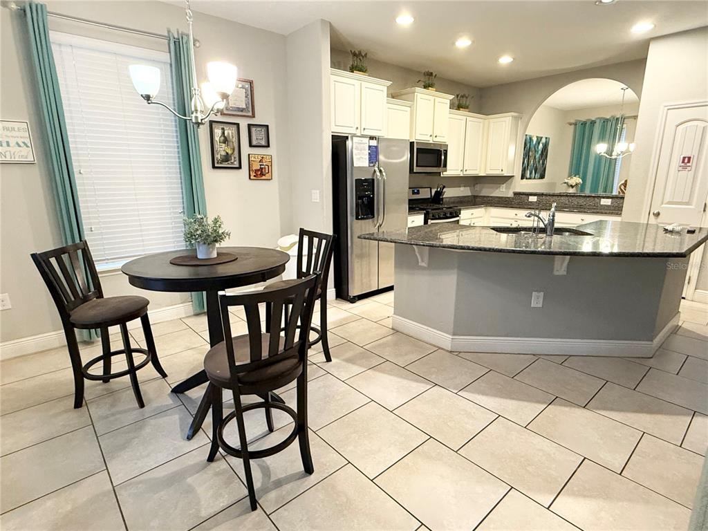 A kitchen features white cabinets, granite countertops, a breakfast nook, and light tile flooring — 5294 WILDWOOD WAY, DAVENPORT, FL