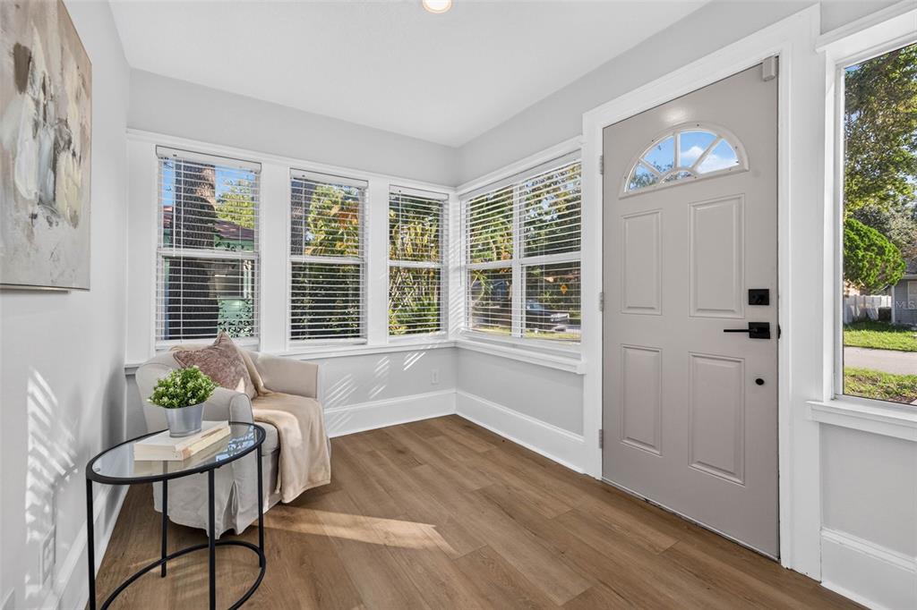 A sunroom with light wood flooring, a gray front door, and a single armchair — 4624 IRIS STREET N, ST PETERSBURG, FL