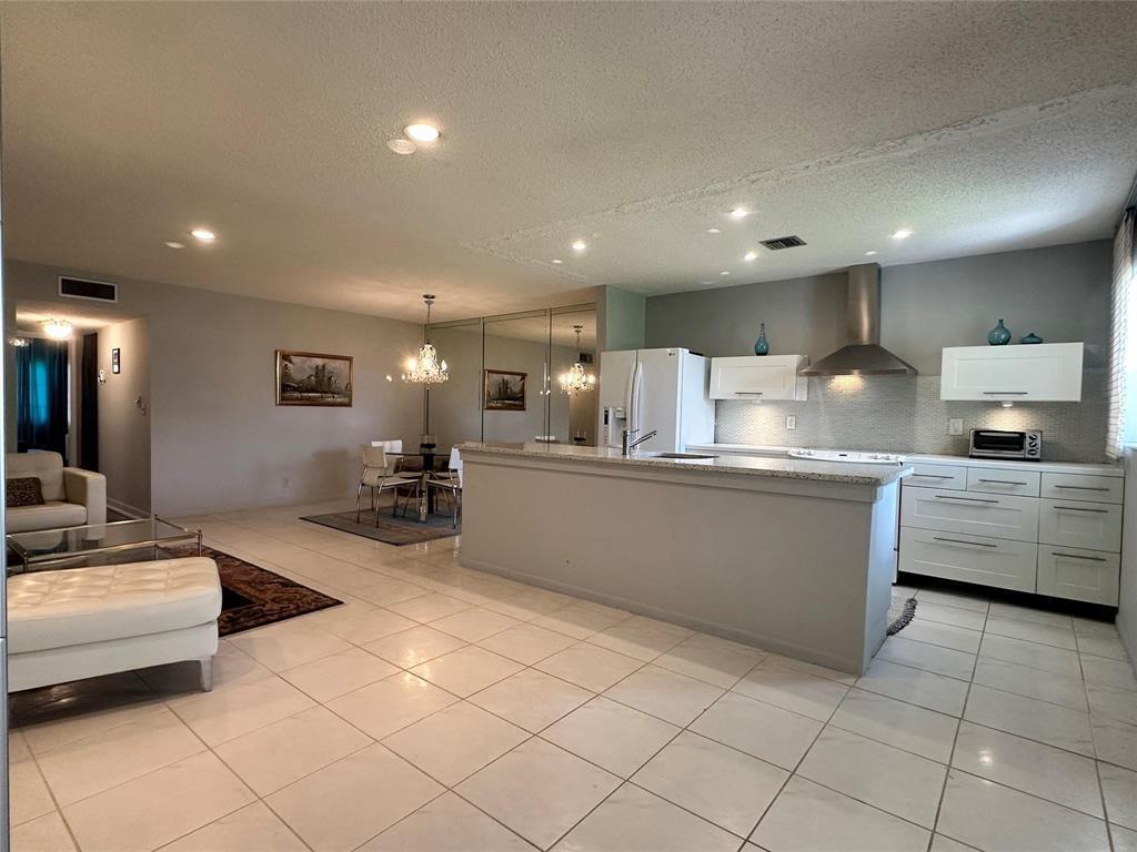 An open-concept kitchen and dining area features white cabinets, granite countertops, and tile flooring — 14492 Canalview Drive # B, Delray Beach FL 33484, DELRAY BEACH, FL