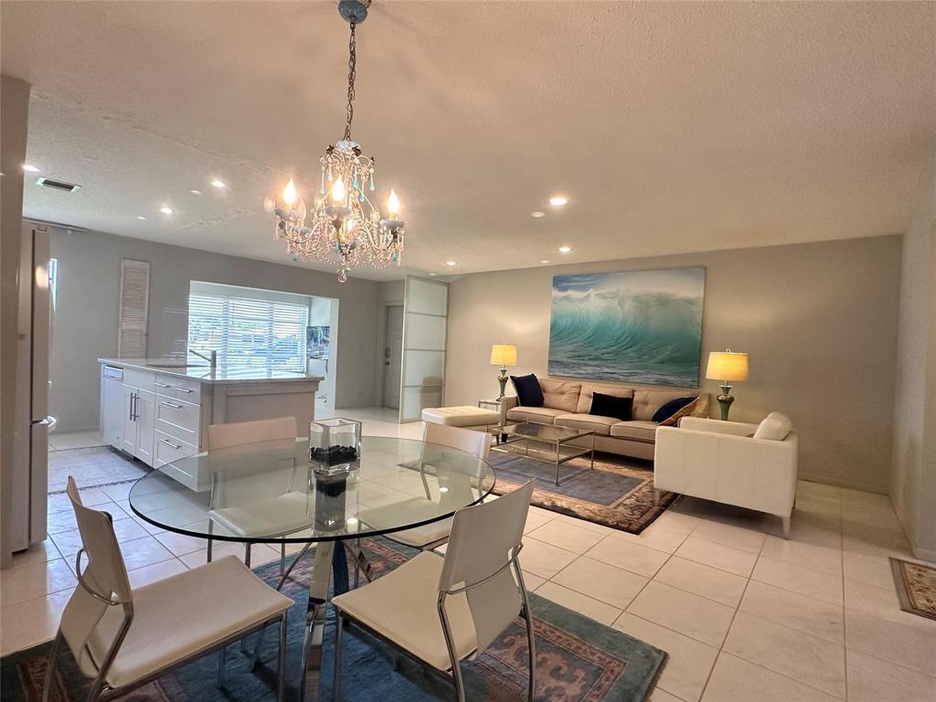 An open-concept living and dining area features a glass table, chandelier, and a large wave painting — 14492 Canalview Drive # B, Delray Beach FL 33484, DELRAY BEACH, FL