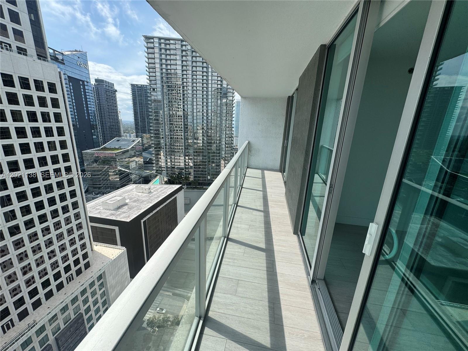 A high-rise balcony features a glass railing, light wood-look tile flooring, and city views — 500 Brickell Ave # 3204, Miami FL 33131, MIAMI, FL