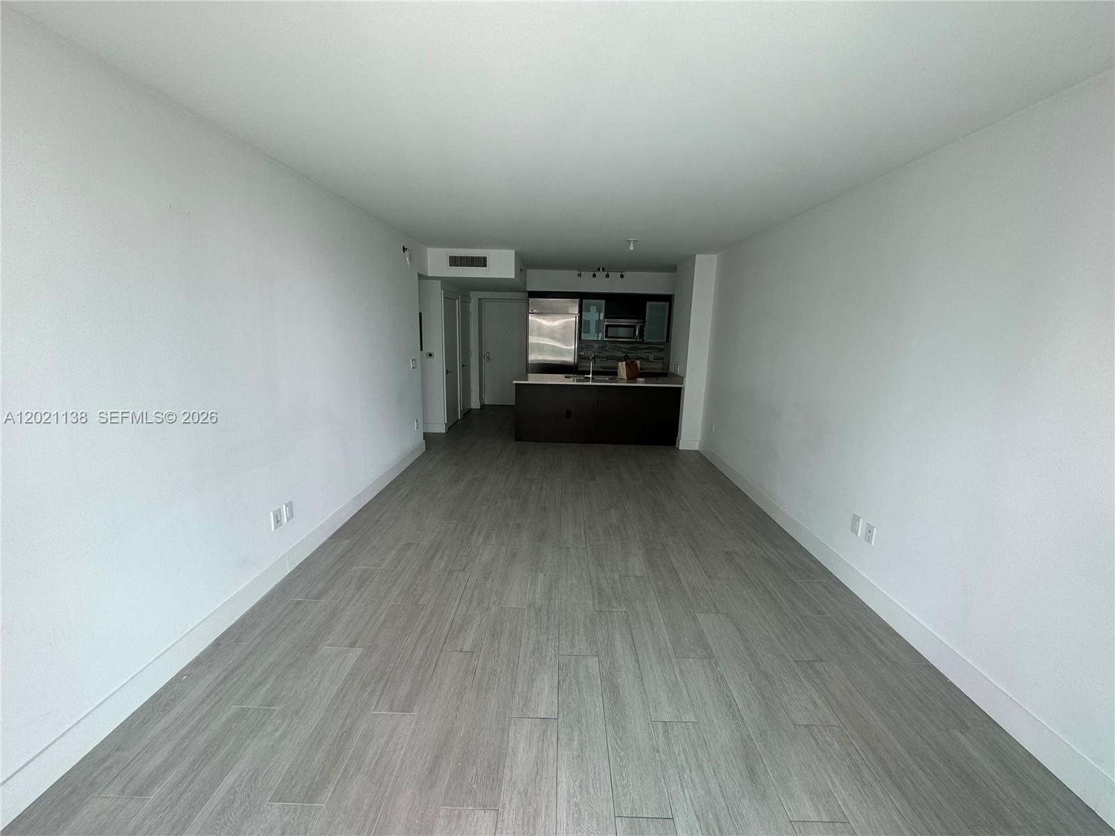 An unfurnished living area with gray wood-look flooring leads to an open kitchen — 500 Brickell Ave # 3204, Miami FL 33131, MIAMI, FL