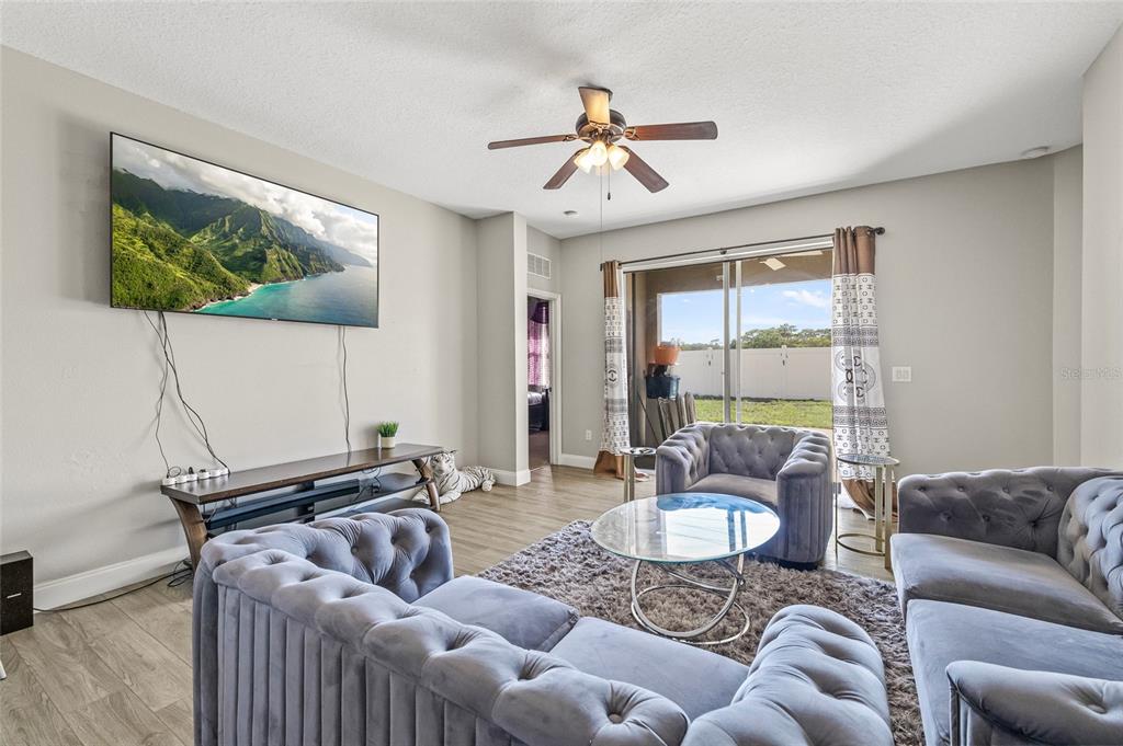A living room features gray tufted sofas, a glass coffee table, and a wall-mounted television — 8521 SOUTHERN CHARM CIRCLE, BROOKSVILLE, FL