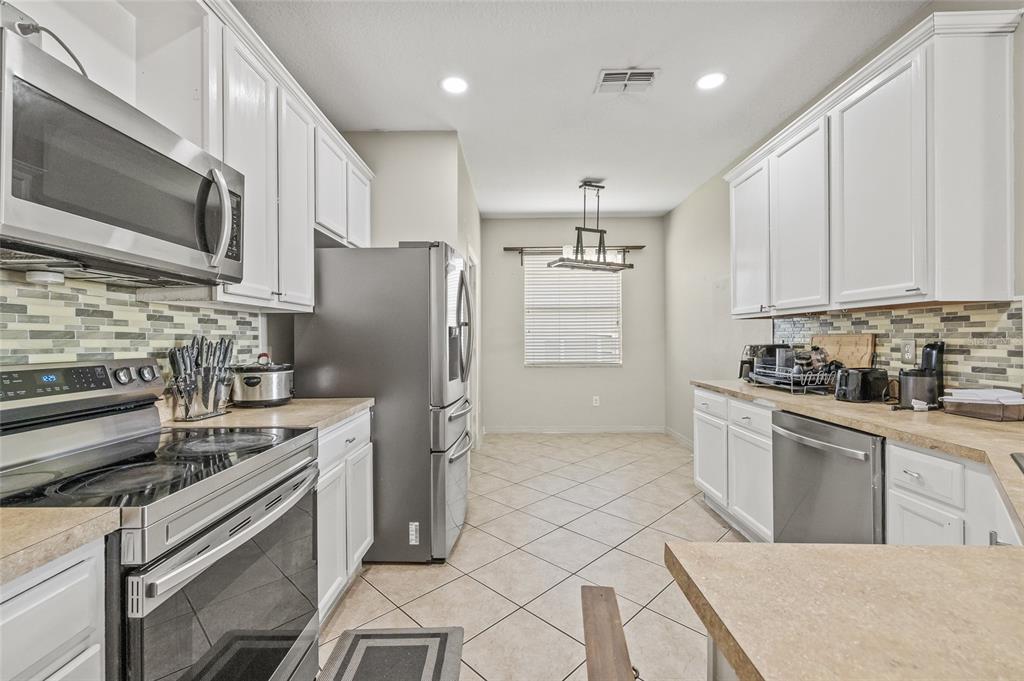A kitchen features white cabinets, stainless steel appliances, a tile backsplash, and a dining area — 8521 SOUTHERN CHARM CIRCLE, BROOKSVILLE, FL