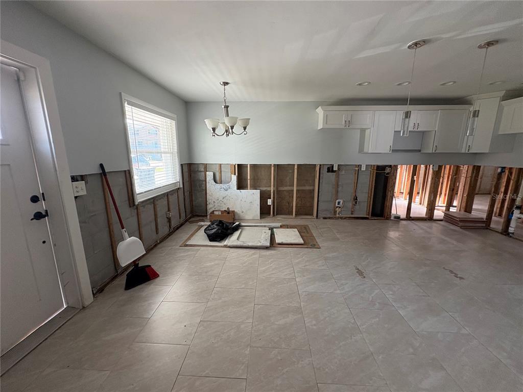 An unfinished kitchen features exposed wall studs, white upper cabinets, and light-colored floor tiles — 6711 S FAUL STREET, TAMPA, FL